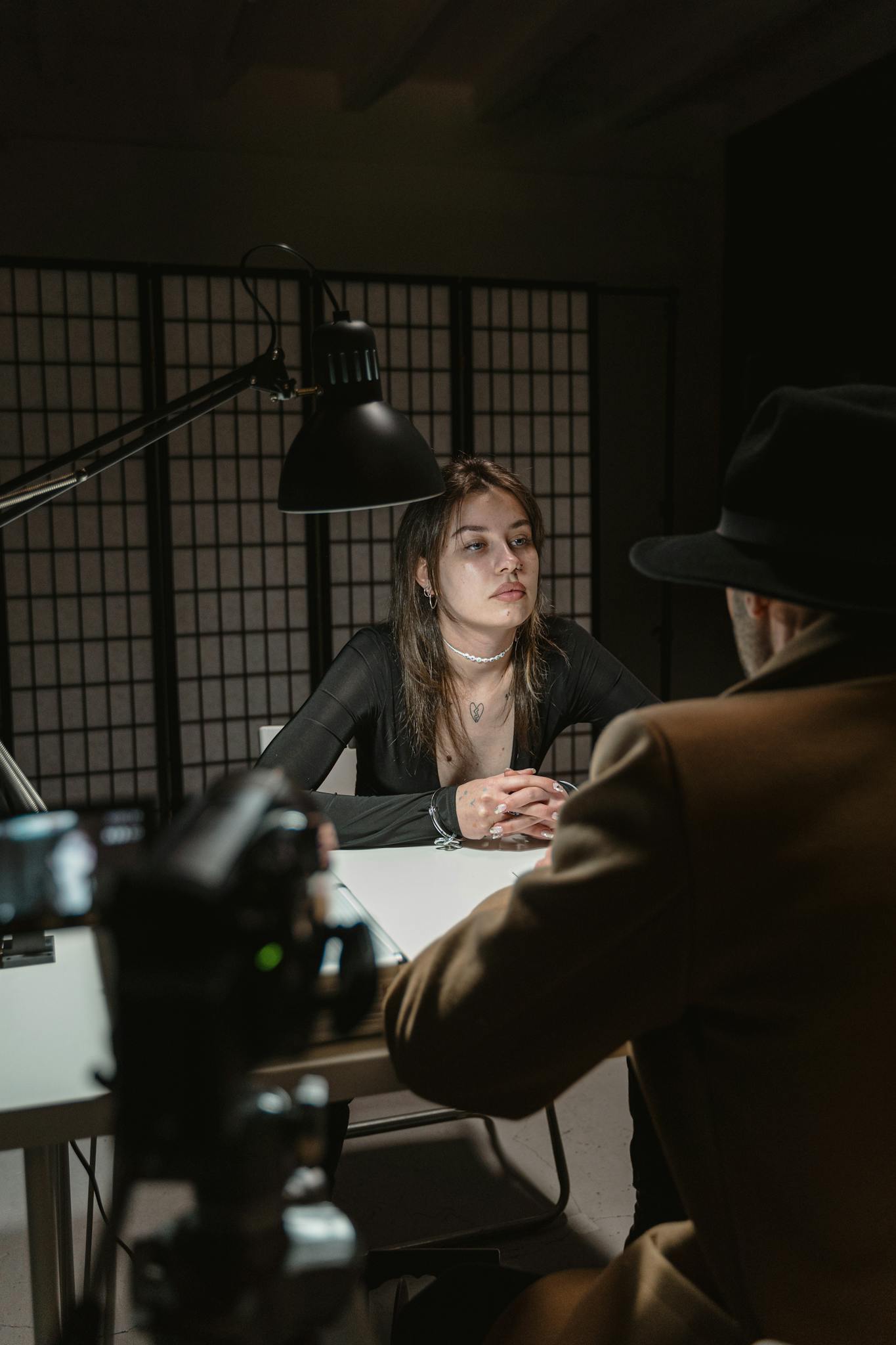 A woman and an investigator in a tense, dimly lit interrogation room.