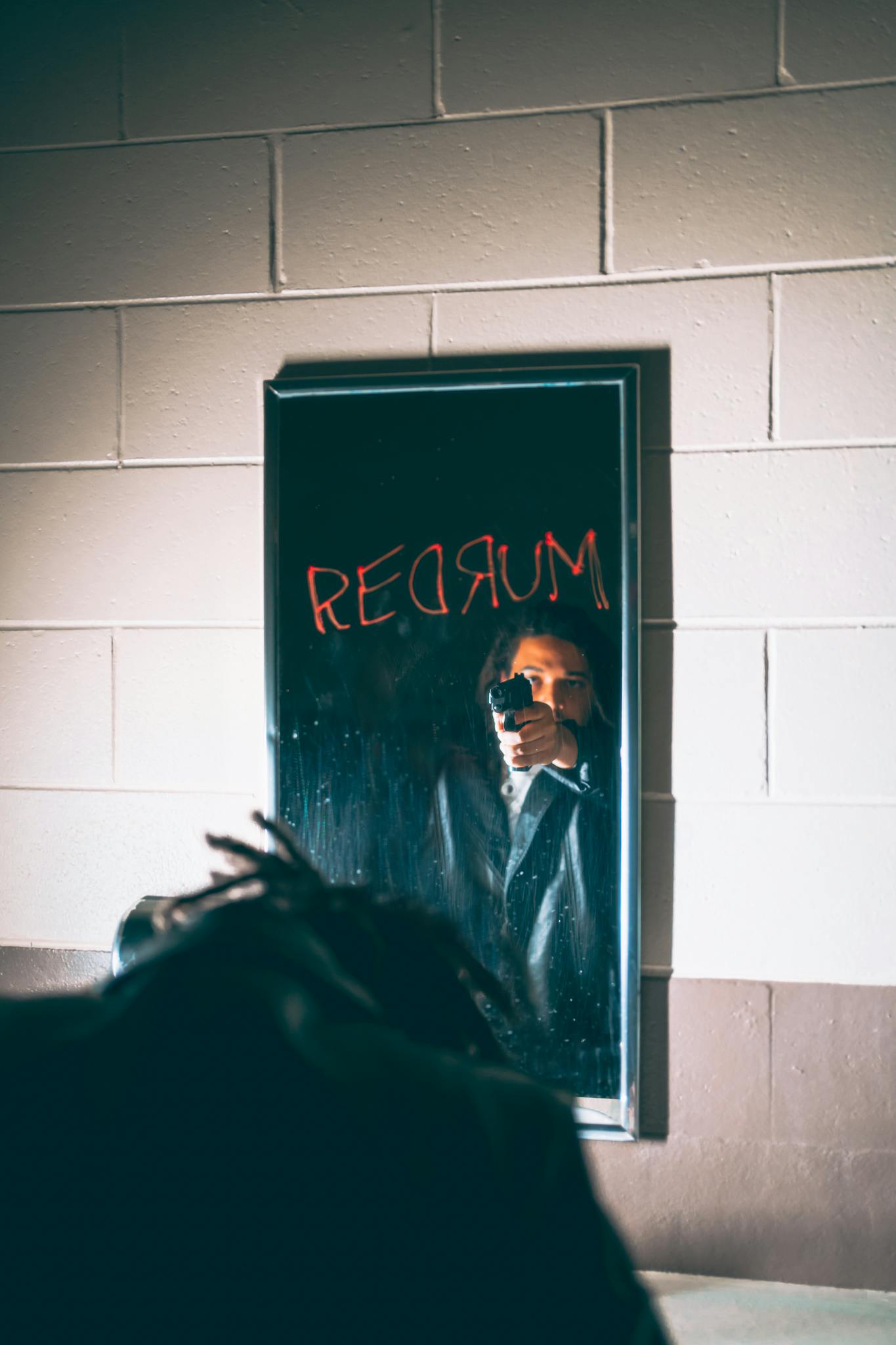 Eerie reflection of a person with a gun and 'Redrum' graffiti on mirror.