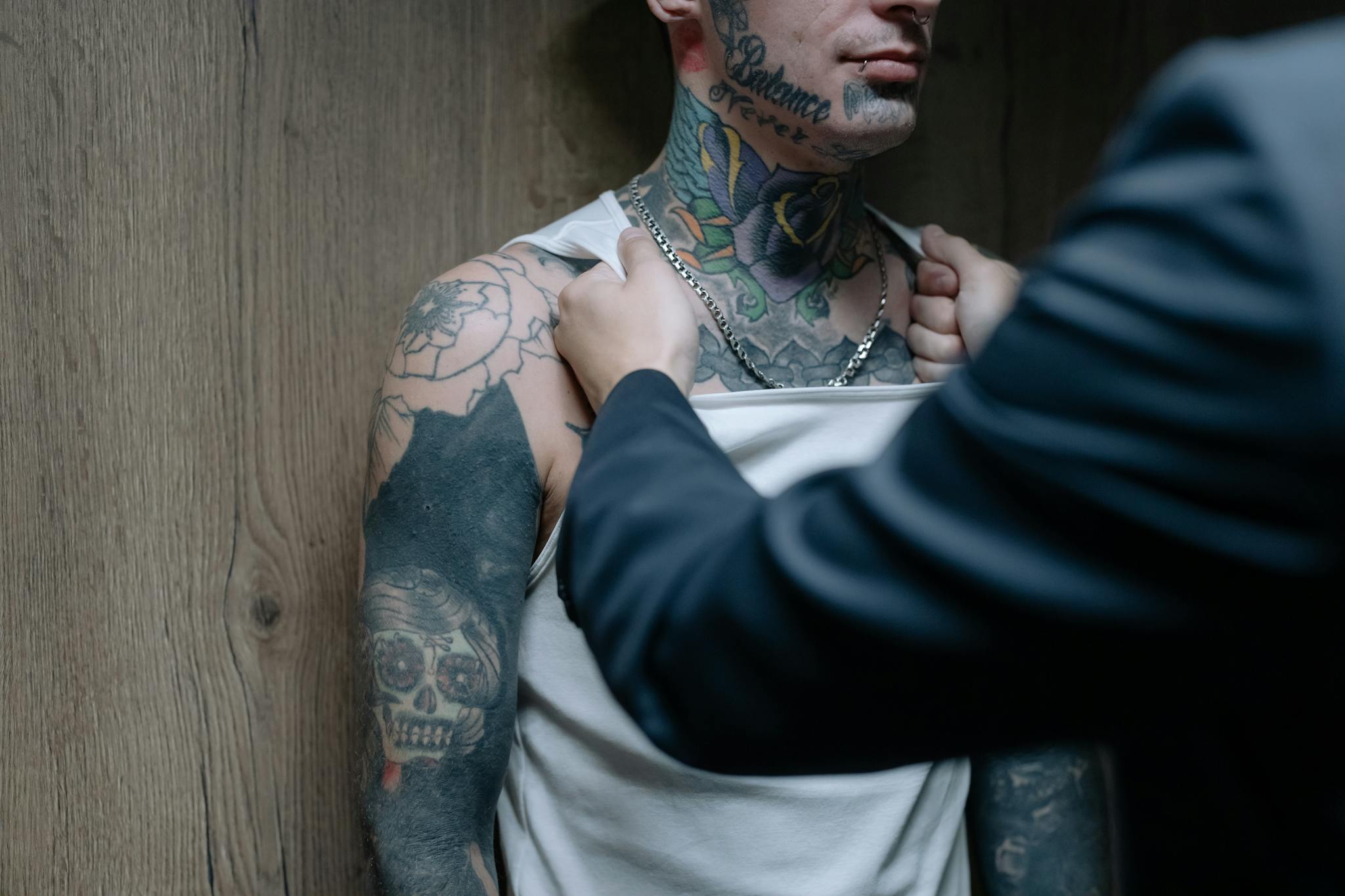 Tattooed man being grabbed by a detective in an intense indoor scene.